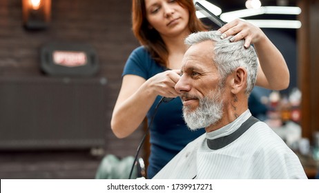 Side view of happy handsome bearded man getting haircut at barbershop. Young barber girl working with hair clipper. Barbershop. Beauty salon. Barber tools. Mens haircut - Powered by Shutterstock