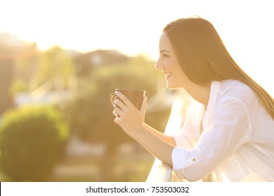 Side View Of A Happy Home Owner Relaxing Drinking Coffee In A Balcony At Sunset