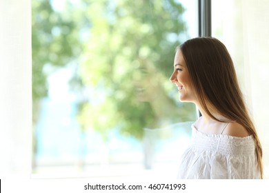 Side View Of A Happy Lady At Home Looking Outdoors Through A Window Of A Living Room Or Bedroom With A Sunny Green Background