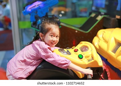 Side view of happy little Asian kid girl playing arcade video game. Motorcycle Racing.