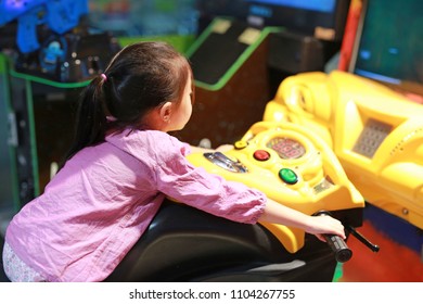 Side view of happy little Asian kid girl playing arcade video game. Motorcycle Racing.