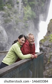 Side View Of A Happy Middle Aged Man And Woman Looking At View Against Waterfall