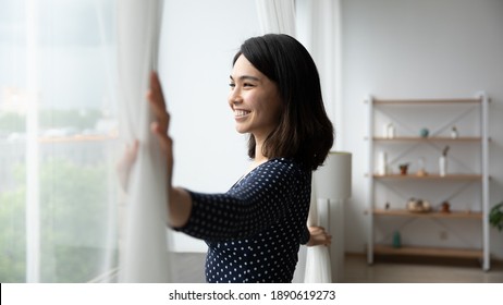 Side View Happy Millennial Asian Korean Woman Opening Curtains, Admiring Morning Cityscape View, Smiling Beautiful Lady Enjoying Peaceful Morning Time, Woke Up Early On Weekend Starting New Day.