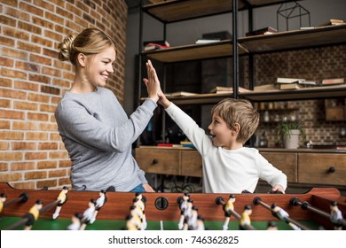 Side View Of Happy Mother And Son Giving High Five To Each Other While Playing Table Football Together At Home