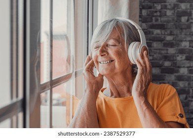 Side view happy old mature retired woman listening popular music in headphones, relaxing alone looking thought window, enjoying peaceful carefree weekend time alone at home, stress free leisure  - Powered by Shutterstock