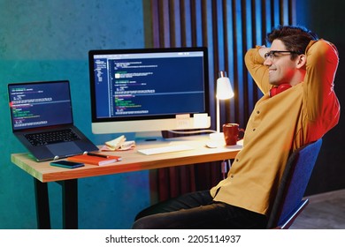 Side View Happy Satisfied Young Software Engineer IT Specialist Programmer Man In Shirt Work At Home Writing Code On Laptop Pc Computer Sit At Table Hold Hands Behind Neck. Program Development Concept