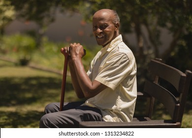Side view of happy senior man hands leaning on a cane while sitting on bench in garden on sunny day 