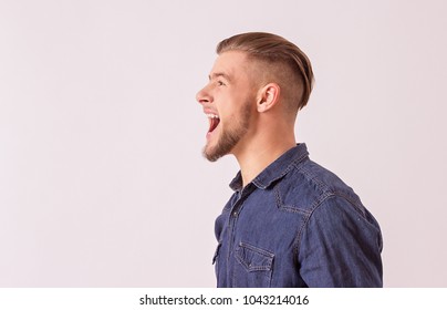 Side view happy, stylish hipster man screaming loudly while isolated on white background with copyspace. Happy bearded man shouting and smiling against white background. Expressing positive emotions