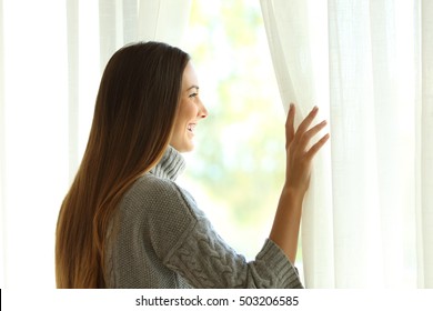 Side View Of A Happy Woman Opening Curtains Of A Window And Enjoying A New Day With A Warm Light From Outdoors