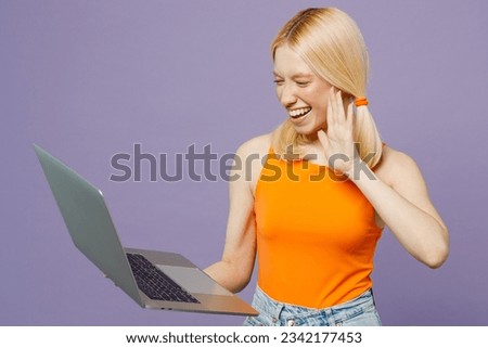 Side view happy young blonde IT woman wear orange tank shirt casual clothes hold use work on laptop pc computer waving hand isolated on plain pastel light purple background studio. Lifestyle concept
