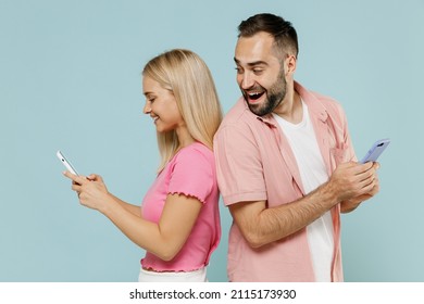 Side View Happy Young Couple Two Friends Family Man Woman In Casual Clothes Peep Hold Use Mobile Cell Phone Stand Back To Back Together Isolated On Pastel Plain Light Blue Background Studio Portrait