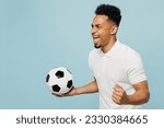 Side view happy young man fan wears basic t-shirt cheer up support football sport team hold soccer ball watch tv live stream do winner gesture clenching fists isolated on plain blue background studio