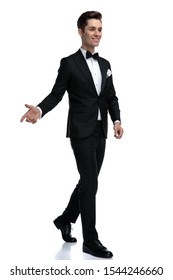 Side View Of Happy Young Man In Tuxedo Looking To Side, Inviting And Greeting, Walking Isolated On White Background, Full Body