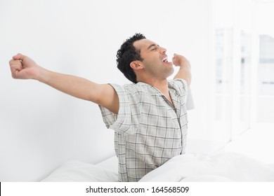 Side view of a happy young man waking up in bed and stretching his arms