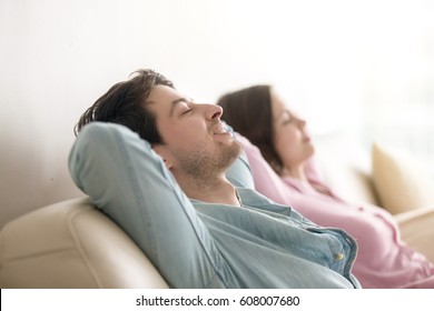 Side View Of Happy Young Man And Woman Enjoying Sitting On Sofa At Home, Relaxing With Eyes Closed, Resting Hands Behind The Head, Breathing, Dreaming Of Vacation, Imagining, Leisure Lazy Day