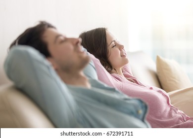 Side View Of Happy Young Man And Woman Enjoying Sitting On Sofa At Home, Relaxing With Eyes Closed, Resting Hands Behind The Head, Recreating, Dreaming Of Vacation, Imagining, Leisure Lazy Day