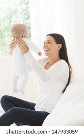 Side View Of A Happy Young Woman Lifting Little Baby In Bed