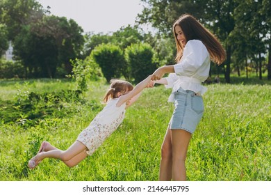 Side View Happy Young Woman Wear White Clothes Have Fun Child Baby Girl 5-6 Years Old Arms Mommy Play Rest With Little Kid Swinging Daughter By Hands Spend Time Outdoor Together. Love Family Concept