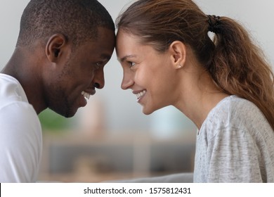 Side view head shot close up image happy smiling affectionate mixed race family couple touching foreheads, bonding looking at each other eyes, enjoying tender moment, showing love, support at home.