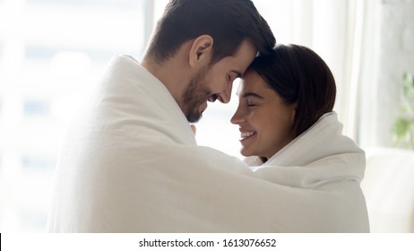 Side View Head Shot Close Up Young Bonding Family Couple Covered In Warm Cozy Blanket Touching Foreheads, Enjoying Intimate Tender Moment. Happy Married Spouse Spending Sweet Morning Time Together.