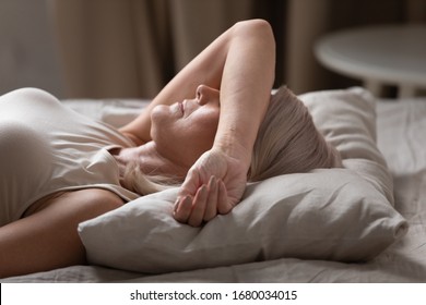 Side view head shot close up middle aged woman lying in bed at home or hotel, covering eyes with arm, trying falling asleep at night or protecting herself from disturbing bright daylight in morning. - Powered by Shutterstock