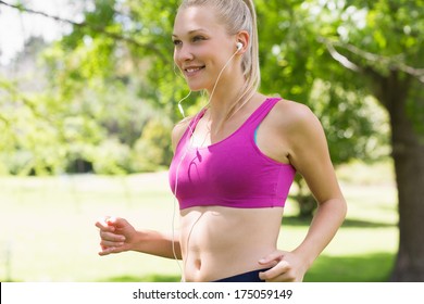 Side view of a healthy and beautiful young woman in sports bra jogging in the park