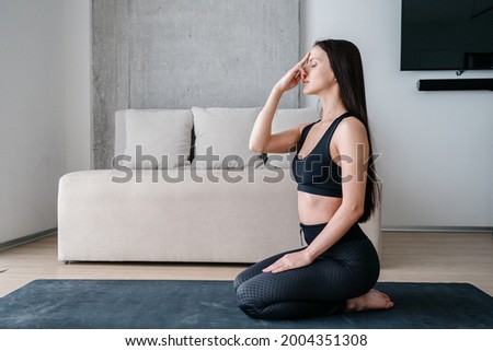 Side view of healthy brunette woman touching her nose while doing alternate nostril breathing exercise after meditation during yoga practice at home. Healthy lifestyle concept