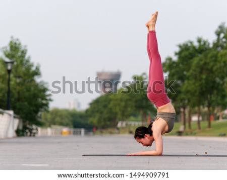 Side view of healthy women in sportswear, red pants and top practicing yoga outdoor, doing handstand exercise on yoga mat salamba sirsasana pose, full length portrait.
