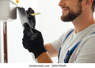 Side View Of Heating Fitter In Protective Gloves Making Notes While Checking Gas Consumption At Gas Pipe And Meter Counter