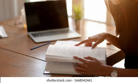 Side View Of High School Or College Students Reading Book To Find Information On Wooden Desk 