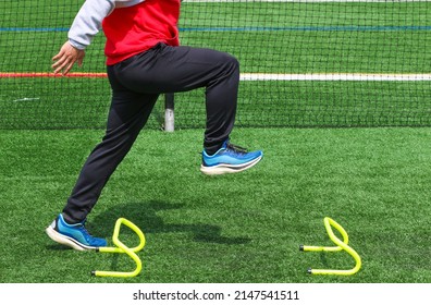 Side view of a high school track runner standining in the track A position over a small yellow hurdle doing sports training drills. - Shutterstock ID 2147541511