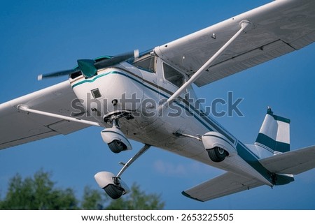 Side view of a high-wing Cessna light aircraft climbing out after lifting. The propeller is in motion, and the landing gear is visible. The aircraft is set against a vivid blue sky.