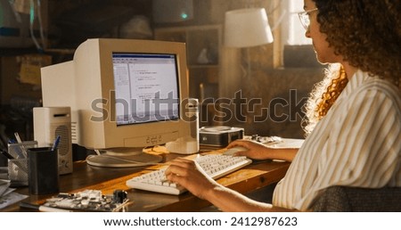 Side View Of Hispanic Female Engineering Student Writing Academic Thesis On Old Desktop Computer In Retro Garage. Future Engineer Focused On Innovative Project For University Of Technology In Nineties