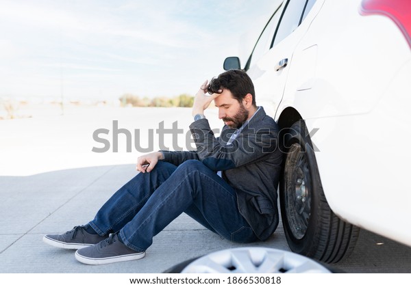 Side view of a\
hispanic guy looking upset and waiting for road assistance to\
change his flat tire 