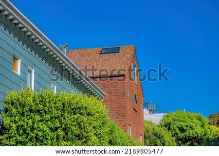 Side view of houses with stylish exterior at San Francisco, CA. There is a house with gray lined walls and decorative corbels and dentils near the house with wood shingles wall and roof with window.