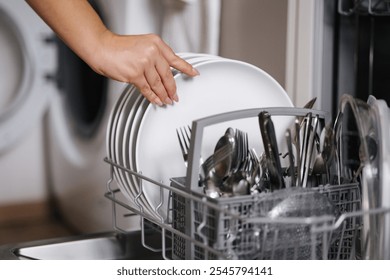 Side view of human hand removing clean plates from a loaded dishwasher. Background of open wash machine 