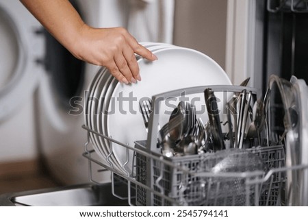 Side view of human hand removing clean plates from a loaded dishwasher. Background of open wash machine 
