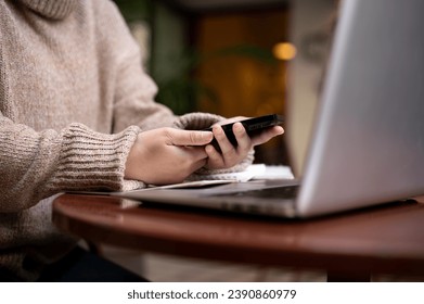 Side view image of a woman using her smartphone at a table outdoors while working remotely at a cafe in the city. People and technology concepts