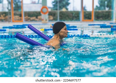 Side view indoor portrait focused caucasian senior woman in a black head cap using violet pool noodle during swimming. Equipment concept. High quality photo - Shutterstock ID 2234697577