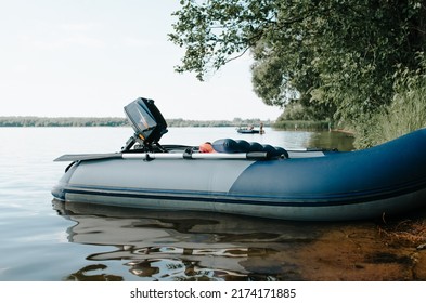 Side view of inflatable motor boat near shore of lake in nature. Close-up of simple fishing boat with motor and oars on water.
