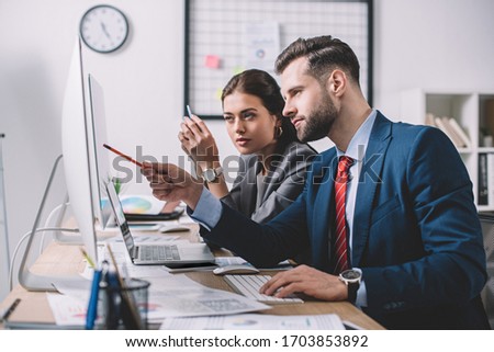 Side view of information security analyst pointing at computer monitor to colleague in office