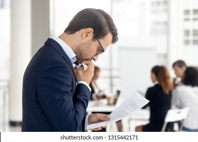 Side View Insecure Male Holding Paper Reading Preparing For Performance Feel Afraid Of Public Speaking, Company Staff Sitting At Desk In Background. Fear Of Job Interview Fail, Stress At Work Concept