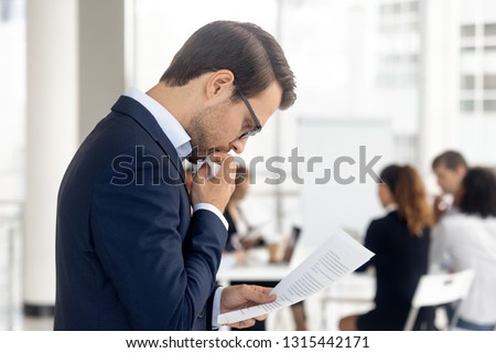 Side view insecure male holding paper reading preparing for performance feel afraid of public speaking, company staff sitting at desk in background. Fear of job interview fail, stress at work concept