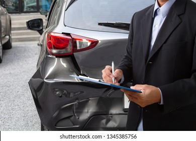 Side view of insurance officer writing on clipboard while insurance agent examining black car after accident.