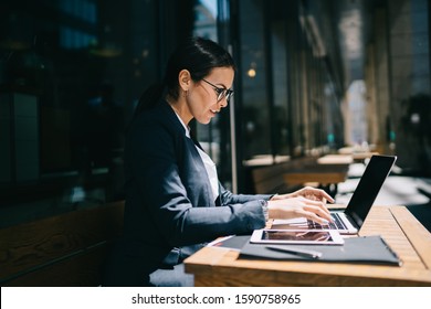 Side View Of Intelligent Businesswoman In Formal Wear Typing On Laptop Keyboard While Sitting At Table Outside Modern Building On City Street