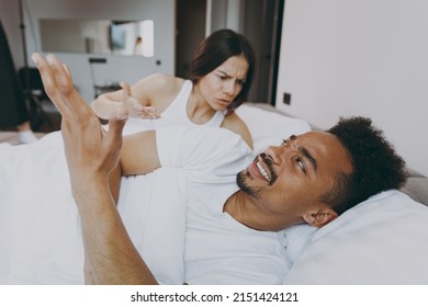 Side view irritated sad angry young couple two family man woman in casual white clothes lying in bed have quarrel scolding screaming spend time together in bedroom lounge home own room house wake up