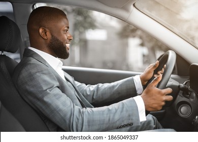 Side View Of Joyful African American Young Man Driver Looking At The Road And Smiling, Copy Space. Happy Black Businessman In Suit Driving Car, Going Home After Successful Working Day