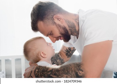 side view of joyful tattooed man and baby boy looking at each other face to face