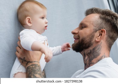 Side View Of Joyful Tattooed Man Holding Baby Boy In Hands