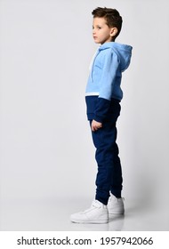 Side View Kid In Blue Warm Overalls, White Sneakers Walking Along The Studio Wall. Full-length Portrait. Children's Fashion, Casual Wear, Comfortable Children Clothing For Winter And Autumn